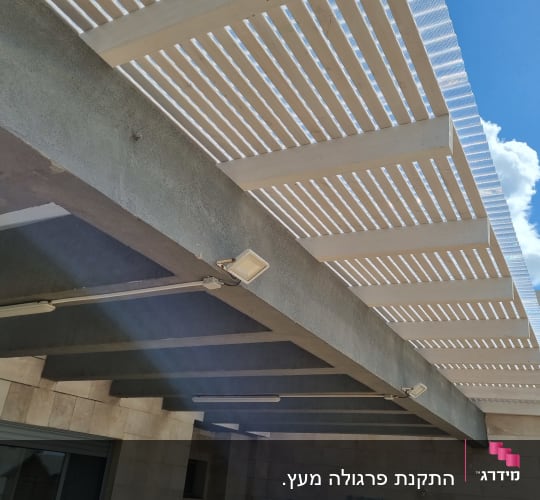פרגולה מעץ עם תאורה חיצונית על קיר אבן